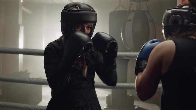 Two young Caucasian women sparring in boxing ring, wearing protective headgear and gloves in slow motion. Perfect for women empowerment campaigns and fitness brand advertisements