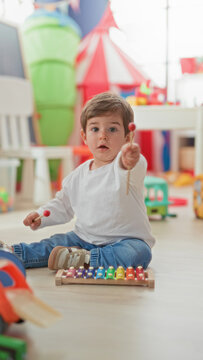 Boy playing xylophone with mallet, hand striking colorful bars in building; concentration early learning.
