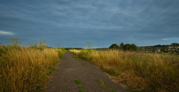 Wolkenstimmung im Fr&uuml;hlicht des Tages an den Feldern mit Weg am Ortsrand auf dem Lande