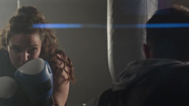Young Caucasian woman boxing with middle aged Caucasian male trainer holding focus mitts in gym. Footage ideal for fitness brand commercials and motivational sports marketing campaigns