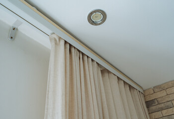 Beige linen curtain with soft folds hanging from decorative painted track under recessed ceiling light in interior corner, with curtain, linen, beige, drapery detail © Aleksey