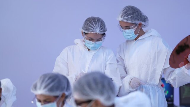 Cleanroom team discusses a silicon wafer and tablet data together during a collaborative semiconductor microchip quality inspection in a sterile hitech manufacturing facility