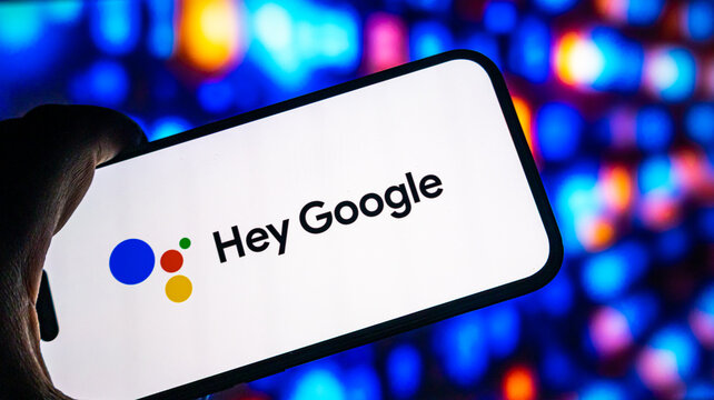 Smartphone displaying google assistant logo against vibrant blurred bokeh background in dark room setting handheld image.