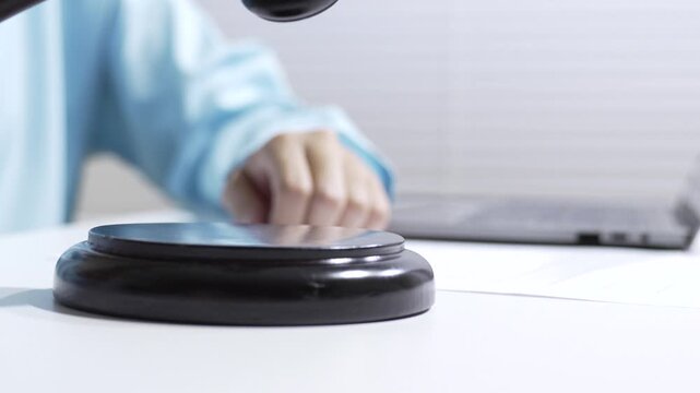 Legal auction gavel table with hand holding document blurred office courtroom formal closeup selective focus, judge hammer base for law trial concept with legal office background and copy space