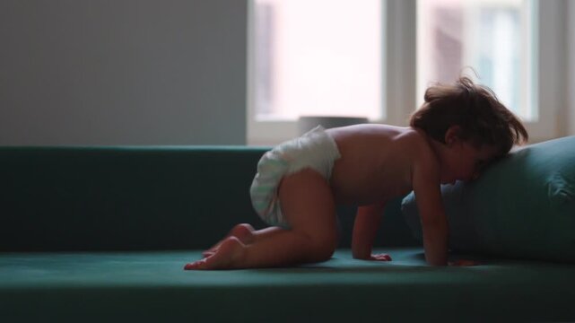 Toddler leaping through the air onto sofa at home, capturing fearless play, physical confidence and joyful childhood adventure