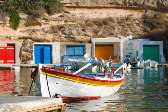 Traditional fishing boat floating in the harbor at Mandrakia, Milos, Greece, surrounded by colorful boat garages and calm coastal waters.