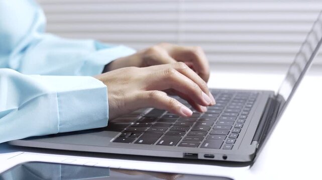 Hands typing on laptop keyboard close up in office work with blue sleeve, computer input on white desk, blurred background, focused technology task