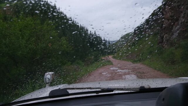 POV shot from inside a vehicle driving on a bumpy dirt road in the mountains during rainfall. Perfect for automotive commercials, travel vlogs, road trip stories, and adventure lifestyle content.