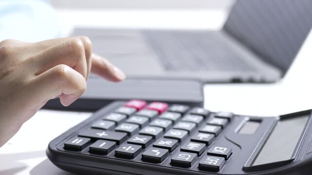 Closeup finger pressing calculator key on office laptop, hand entering number for finance and work, calculator keypad in background with soft light, searchable SEO title