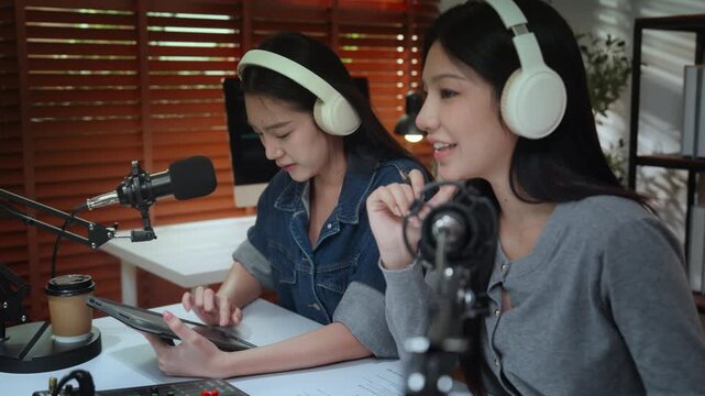 Podcast podcaster influencer creator content microphone headphone recording in cozy studio, female hosts plan episode on tablet, lively conversation and broadcast as coworkers create audio talk show
