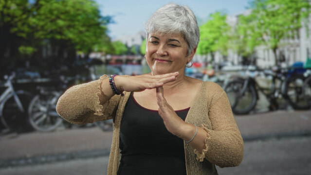 Woman making time out gesture with hands on street by a canal with bicycles and a cardigan visible; warm confidence.