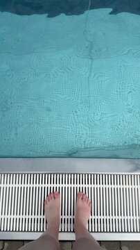 Feet of woman standing near swimming pool top view. Water surface in blue swimming pool close up. Sport, rest, vacation and activity