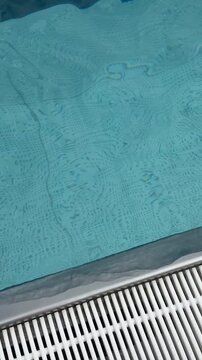 Water surface in blue swimming pool close up. Minimalistic background with waving water and texture of swimming pool bottom tiles. Sport, rest, vacation and activity