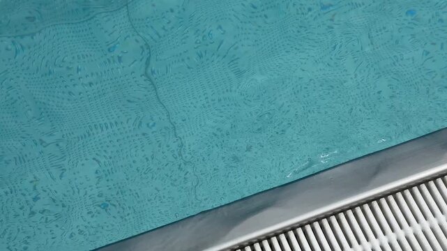 Water surface in blue swimming pool close up. Minimalistic background with waving water and texture of swimming pool bottom tiles. Sport, rest, vacation and activity