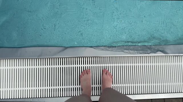 Feet of woman standing near swimming pool top view. Water surface in blue swimming pool close up. Sport, rest, vacation and activity