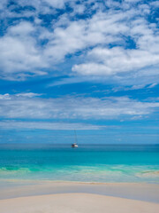 Obraz premium Those colors! The beautiful beach off the coast of Praslin Island. A sailboat in the background. Praslin is an island in the Seychelles.