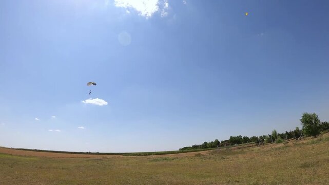 A skydiver landing in an open field amidst picturesque scenery