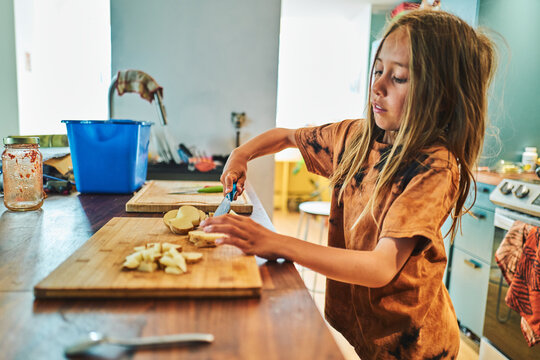 Child standing at a kitchen counter chopping potatoes