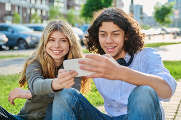 Fototapeta premium Happy teenage friends taking selfie with smartphone outdoors sitting on ground