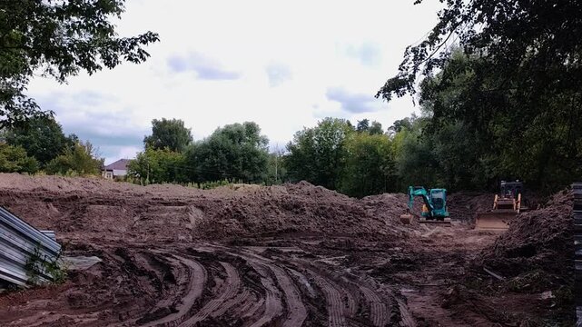 Large and piles at municipal construction site surrounded by forest with two tractors in the background, construction project, heavy equipment, earthmoving operations, infrastructure development