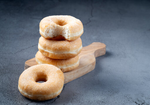 Perspective view of sugar donuts stacked on a wooden cutting board with one donut in the foreground on a gray background