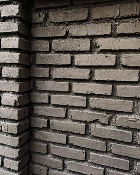 Close-up shot of a rustic painted grey brick wall corner showing rough texture, mortar lines, and dark side lighting. Ideal for industrial interior background, urban architectural design, 3D rendering