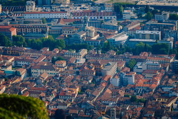 Obraz premium Aerial view of Como city showcasing terracotta rooftops, historic buildings, and green trees under a clear blue sky in northern Italy