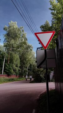 Yield traffic sign beside a quiet suburban road under a dramatic cloudy sky, road safety, transportation infrastructure, traffic regulation, changing weather, summer season.