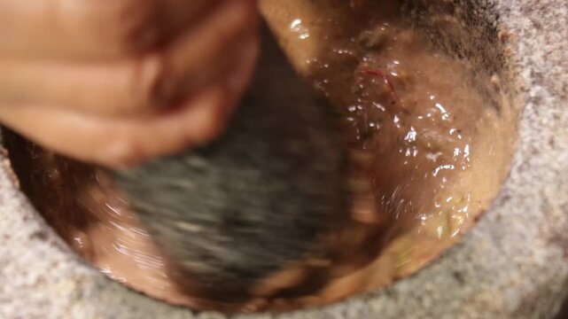 Close-up of crushing ingredients with a granite pestle and mortar to make traditional Nam Phrik Kapi in Bangkok, Thailand.