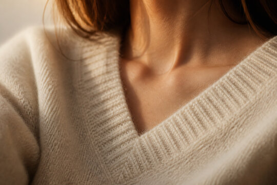 A close-up of a person wearing a cream-colored, V-neck knitted sweater.