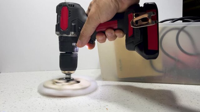 Handyman using a cordless polishing drill to buff and smooth a white marble countertop surface, demonstrating precision craft and professional home improvement work