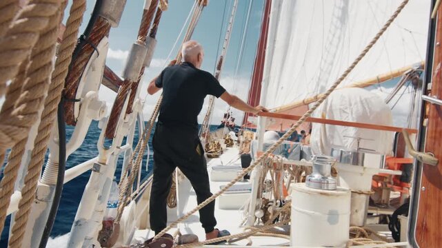Old captain controls the crew working with the sails on the big expeditional sailing vessel moving in the Atlantic Ocean