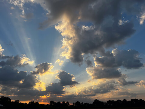 Sunbeams radiating through clouds over silhouetted landscape