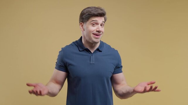 Confused young man shrugging with raised hands in I dont know gesture. Doubt, uncertainty, confusion, indecision and lack of answers concept. Studio portrait on beige background. 