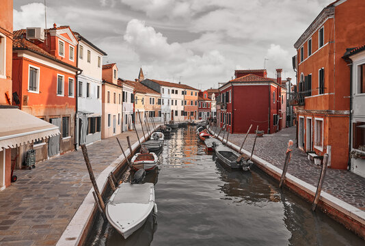 Burano island in Venice Italy picturesque sunset over canal with boats among old colourful houses stone streets..