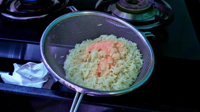 Long-grain rice is seasoned with salt using a fine mesh strainer over a stovetop. The kitchen setting highlights the preparation process with attention to detail.