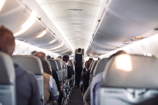 Interior of airplane with passengers on seats and stewardess in uniform walking the aisle, serving people. Commercial economy flight service concept
