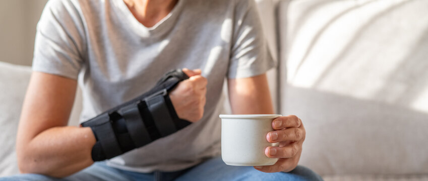 Person wearing a wrist brace for injury or repetitive strain while carefully holding a cup. Managing daily tasks despite pain. Inflammation