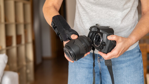 Person experiencing chronic wrist pain and a repetitive strain injury wears an orthosis while preparing to attach a lens to a professional digital single-lens reflex camera