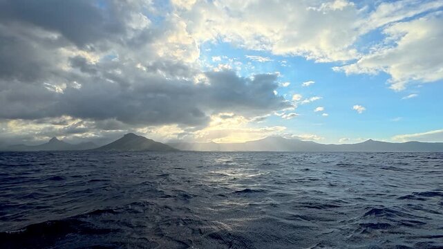 Scenic view of the ocean with mountains in the background under a dramatic cloudy sky with sun rays