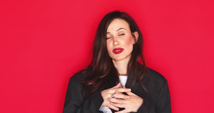 Attractive young woman with long dark hair and vibrant red lipstick explaining something with expressive hand gestures and talking with a serious facial expression isolated on a solid red studio