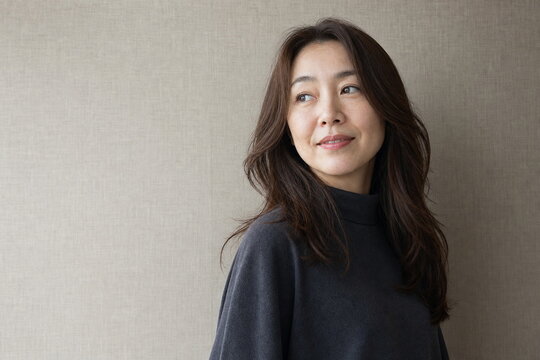 リネン壁の前でロングレイヤーを見せるミドル女性