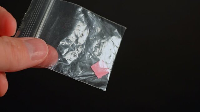 Drug dealer with LSD acid paper squares packed in small bag for sale, controlled drugs. Hallucinogenic psychedelic substances used in party and dance clubs.