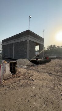 Unfinished concrete building at a dusty construction site during sunset with palm trees.