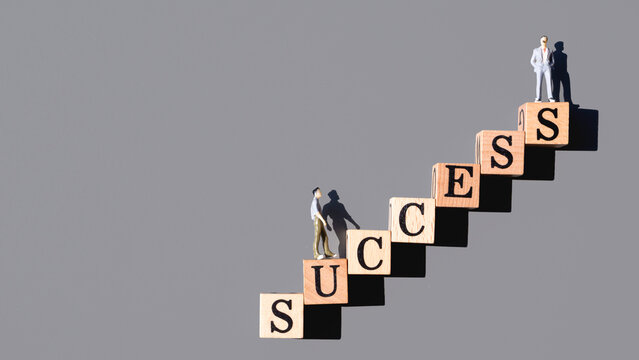 Miniature businessman figures walking up wooden block stairs spelling SUCCESS on gray background, business growth, leadership and career concept.
