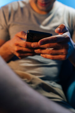 Close-up of man hands holding smartphone. Person scrolling or gaming at night. Modern lifestyle concept with cinematic blue and orange light. Shallow depth of field on mobile device.