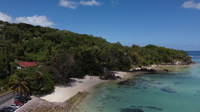 Aerial view of a secluded sandy beach backed by lush jungle and clear shallow lagoon on a sunny day in the Seychelles.