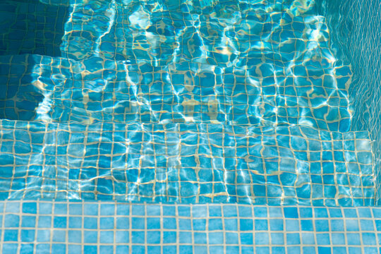 Sunlight dances on blue tiled swimming pool steps underwater