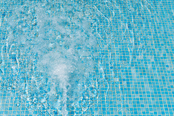Bubbling blue water cascades over a tiled pool surface on a sunny day © Snide12