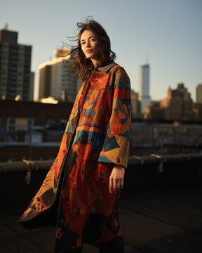 Stylish woman in patterned long coat on city rooftop at sunset